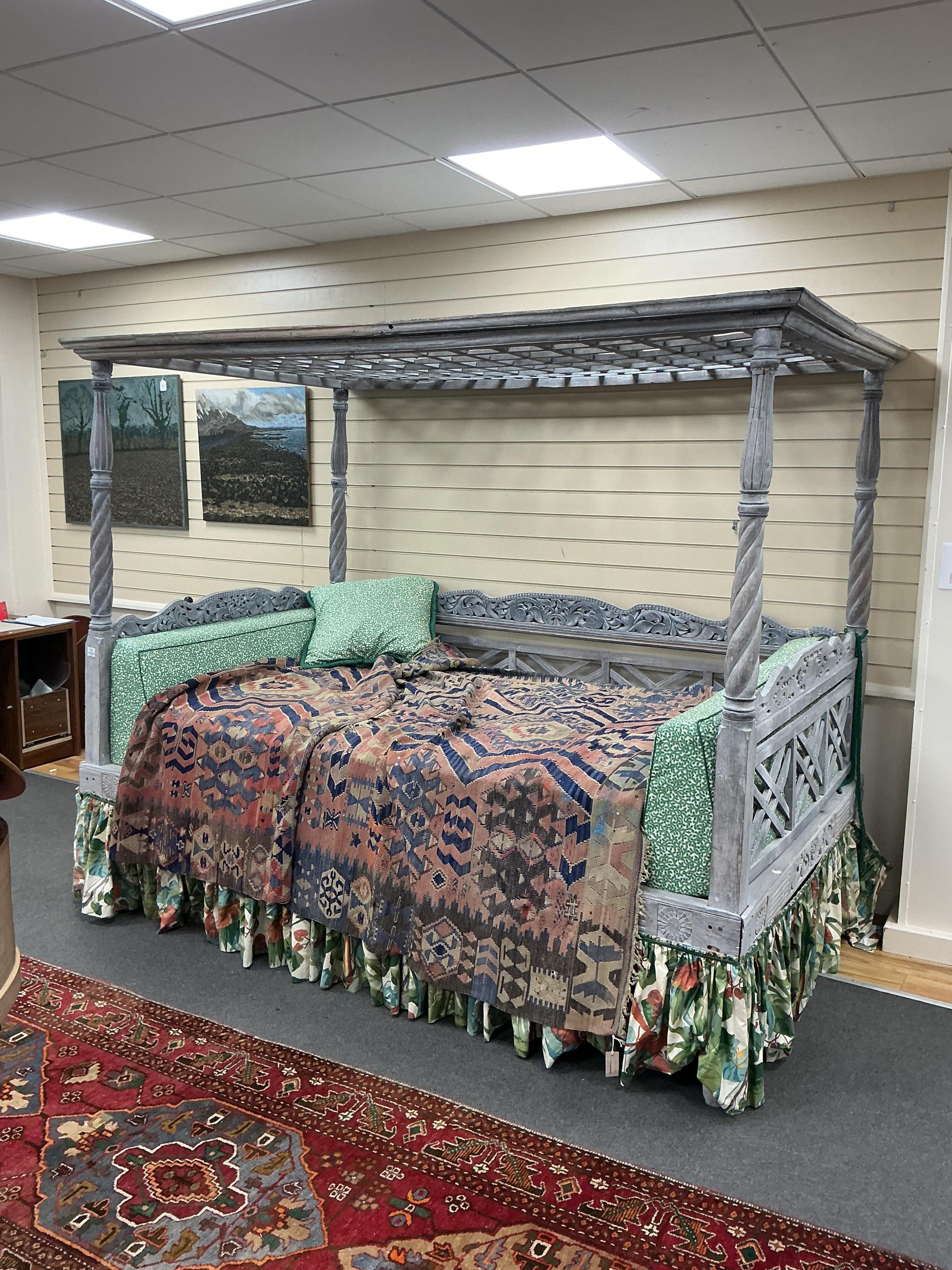 An Indian grey painted carved teak four poster double bedstead, with a pierced canopy over